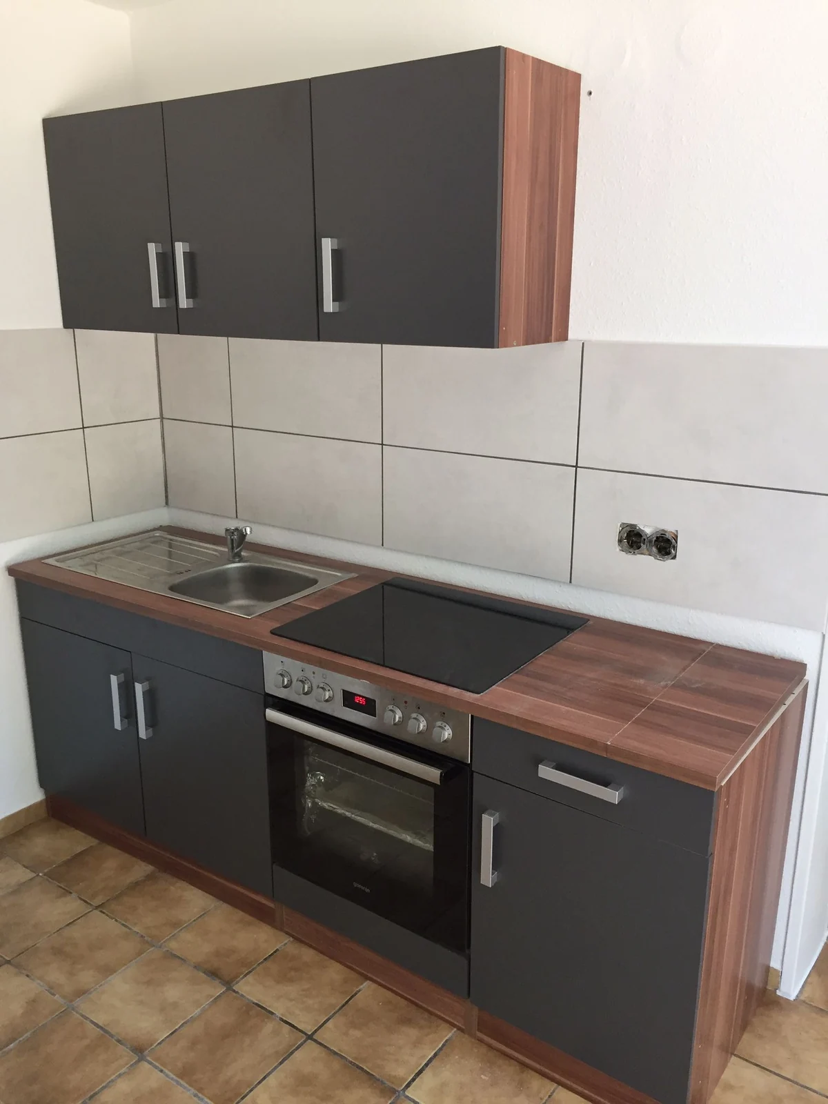 Kompakte Küchenzeile mit dunklen Fronten, Holzdekor, Spüle, Kochfeld und Backofen