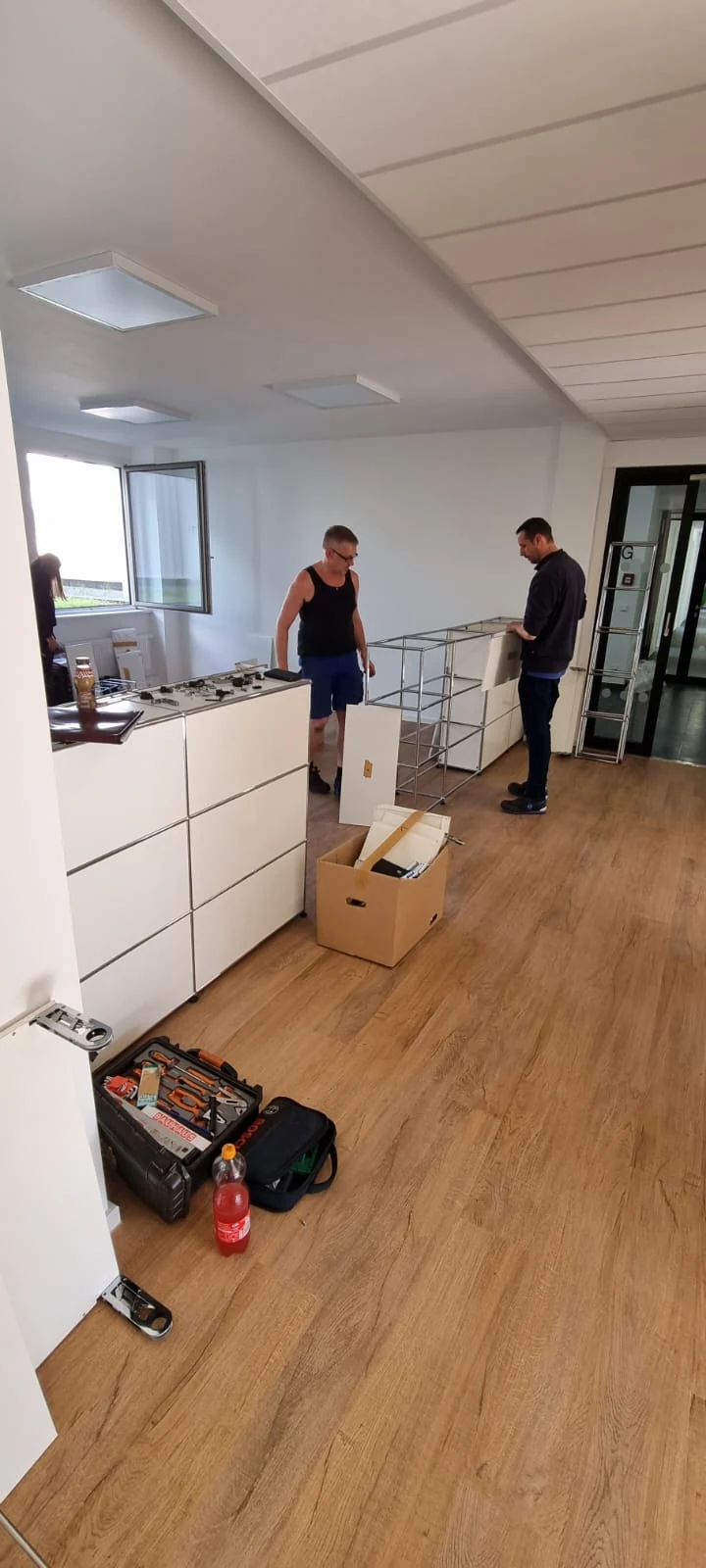 Zwei Monteure bei der Arbeit an weißen USM-Haller-Möbeln mit offenem Chromrahmen